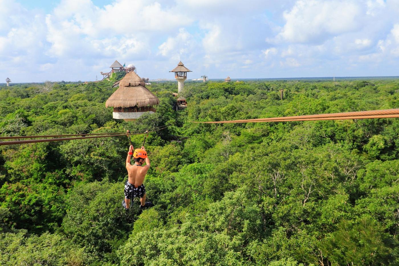 Visitor on a zip line above the jungle canopy at Xplor Park, with the course towers on the horizon, Quintana Roo, Mexico